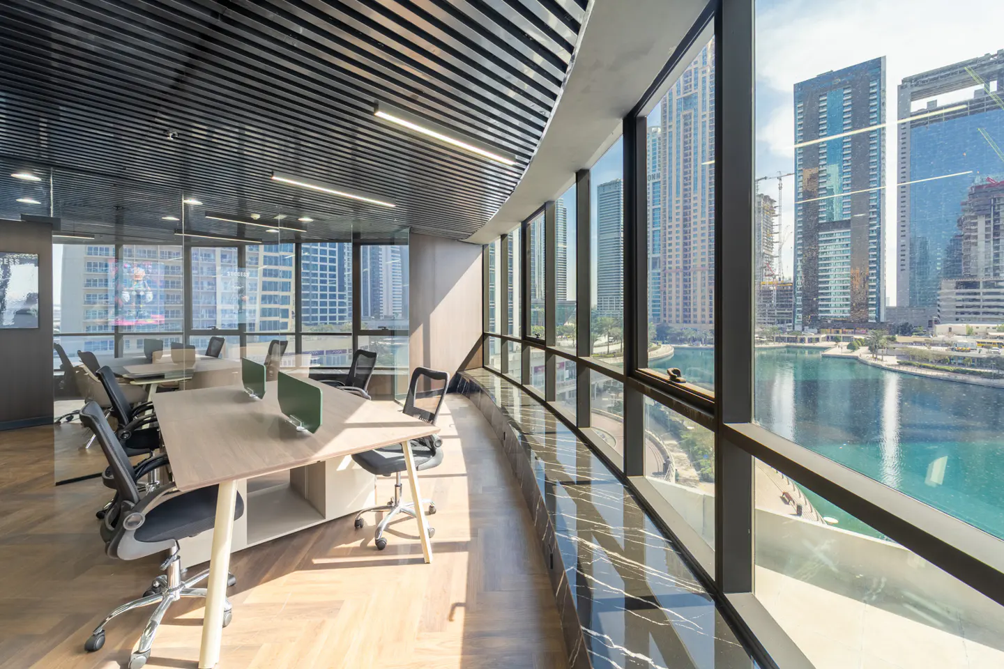 Bright office space with desks, chairs, and a large window overlooking a city skyline and waterway.