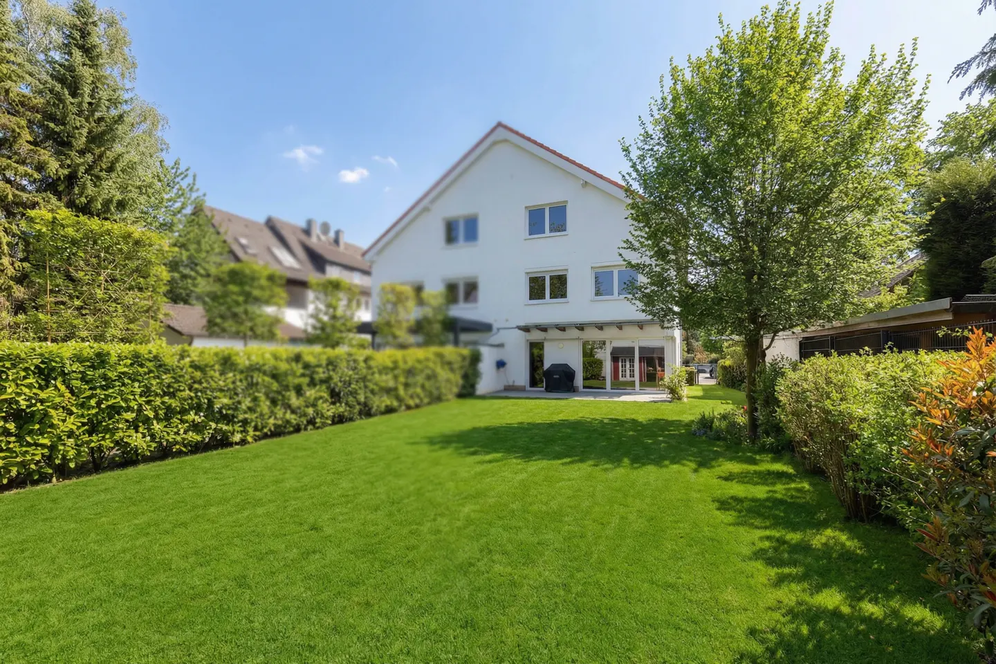 A white two-story house with a green lawn and trimmed hedges under a blue sky.