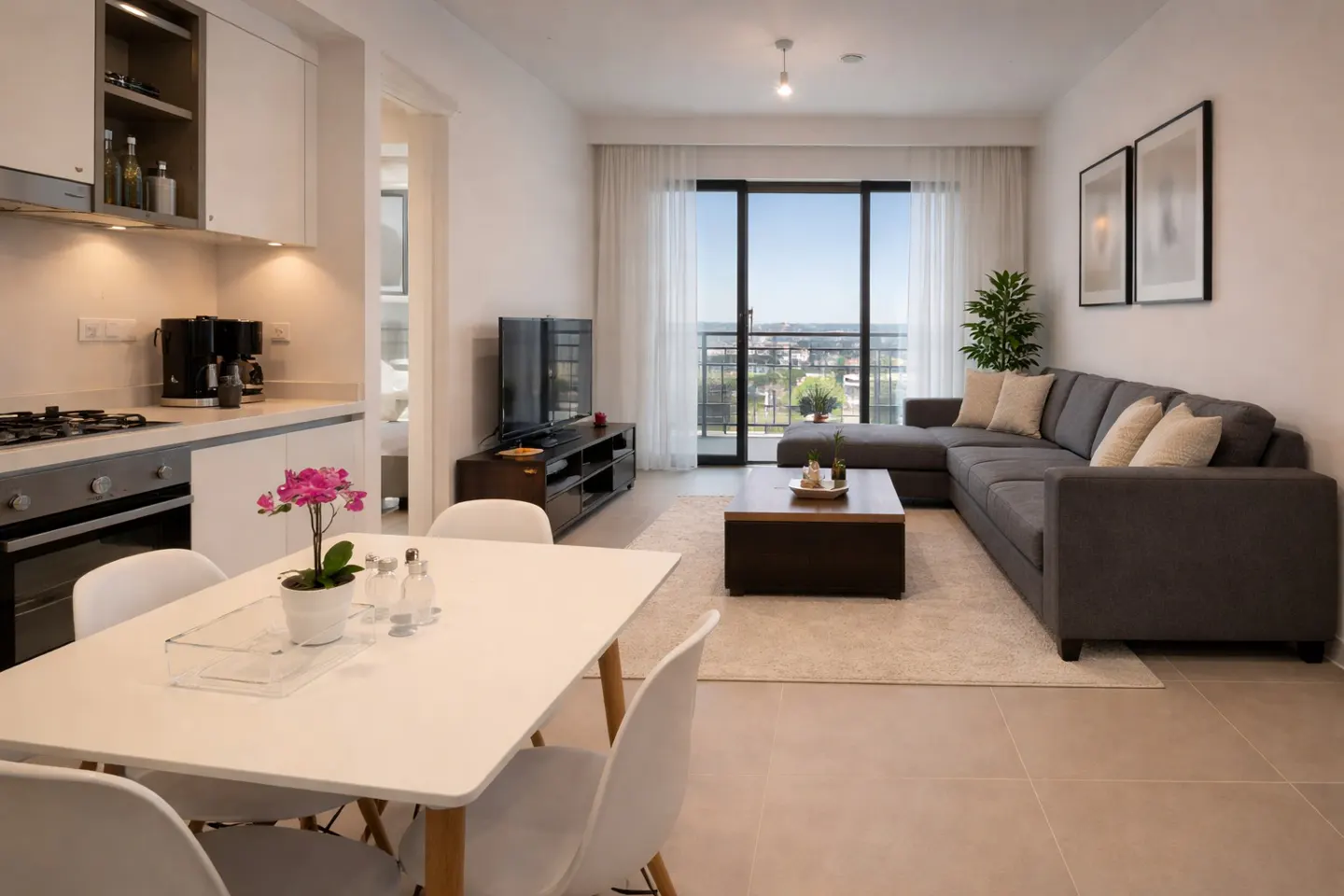 Open-concept living space with a white dining table, gray sectional sofa, and balcony with a city view.