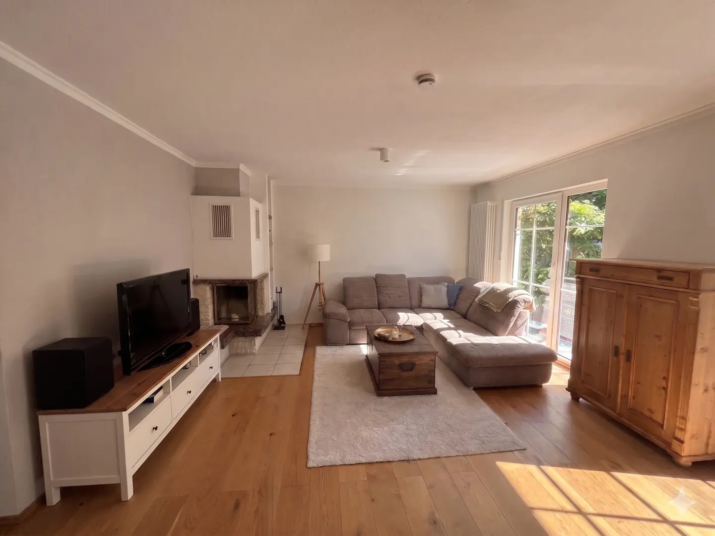 Living room with a brown sectional sofa, wooden coffee table, fireplace, TV, and wooden cabinet on a hardwood floor.