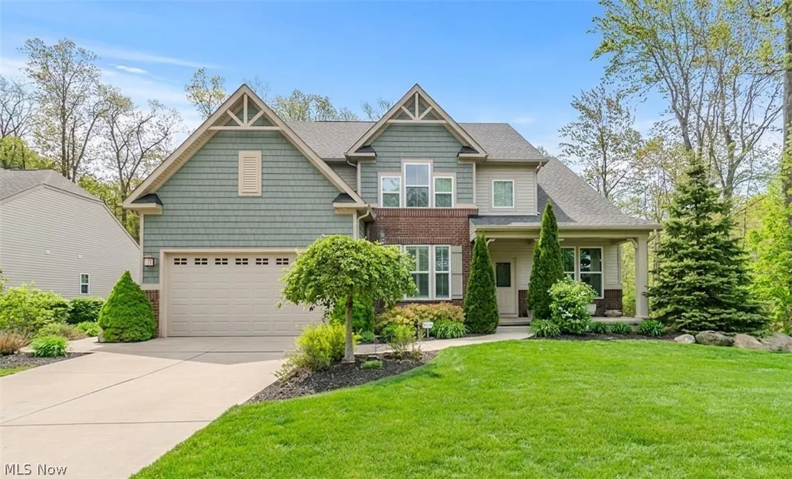 Two-story house with green siding, brick accents, and a gray roof on a sunny day. A green lawn and trees surround the home.