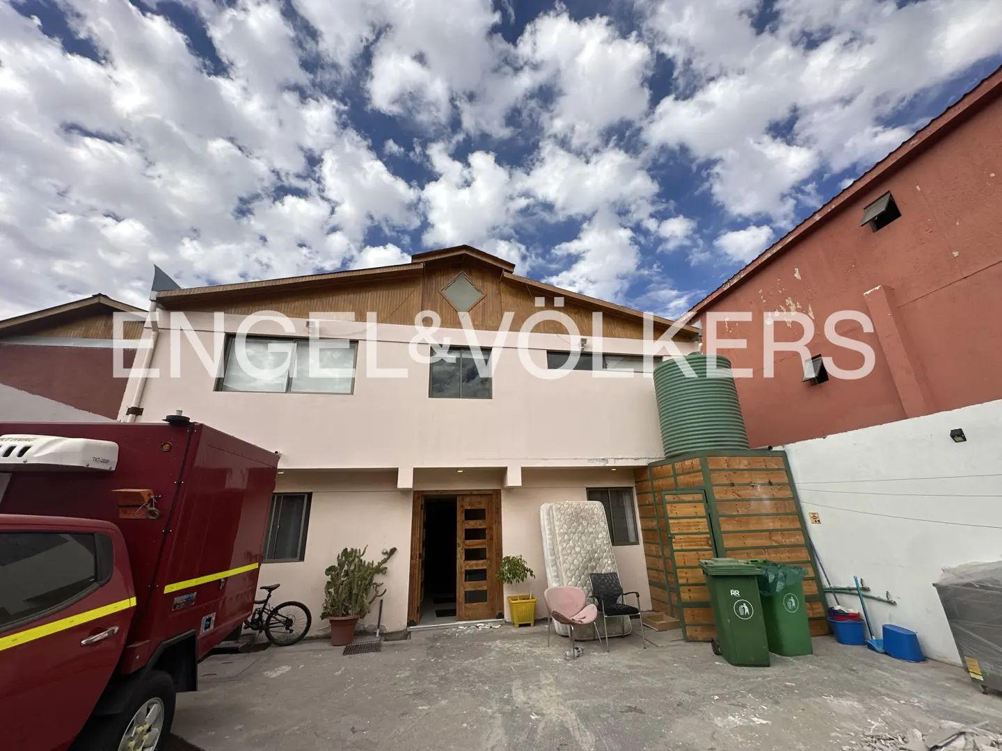 Exterior view of a two-story building with a red truck parked in front, under a cloudy sky.