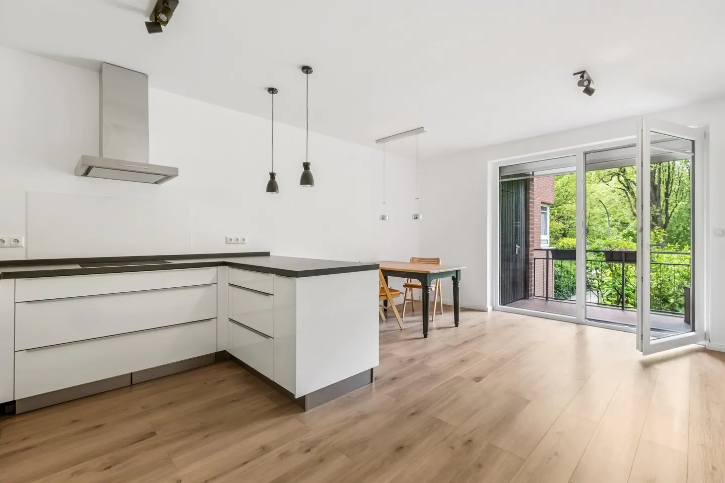 Bright, modern kitchen with white cabinets, black countertops, and wood floors. A dining table sits near open patio doors with a green view.