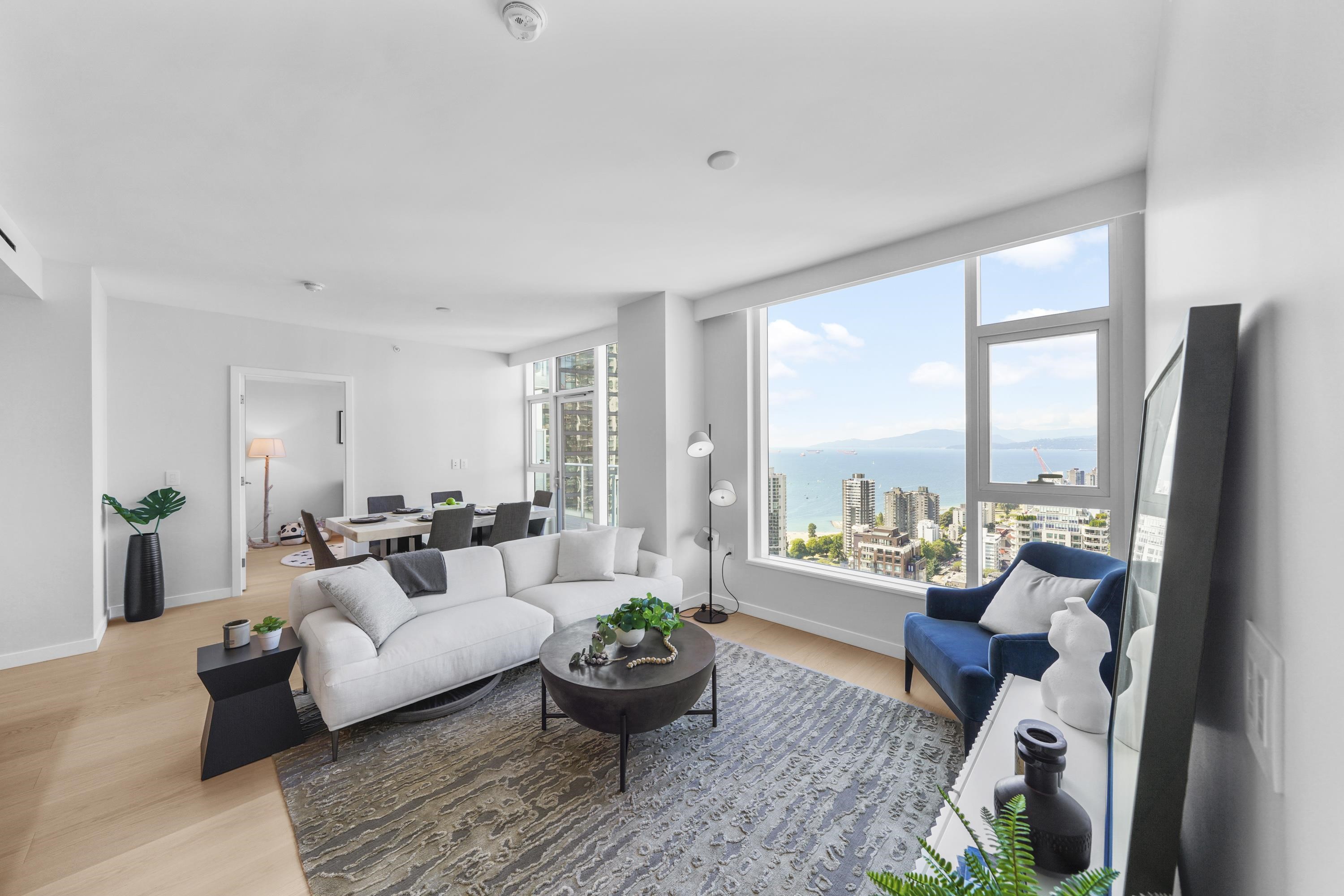 Bright, modern living room with a white sofa, blue chair, and city view from a large window.