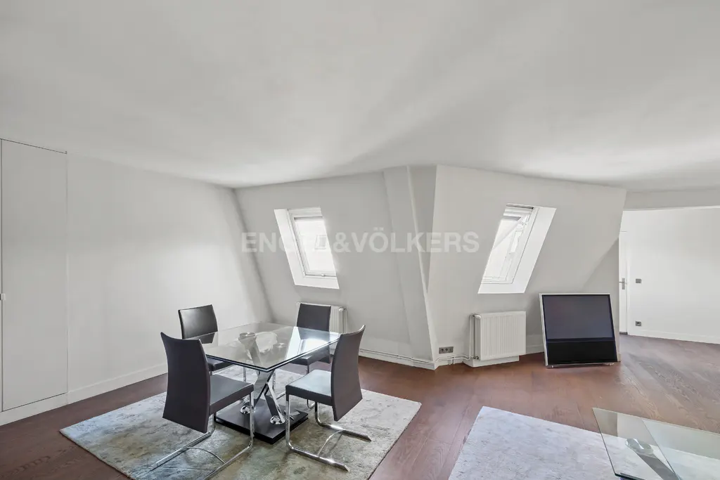 Bright, modern dining area with a glass table, four chairs, and two skylights in a white-walled, wood-floored room.