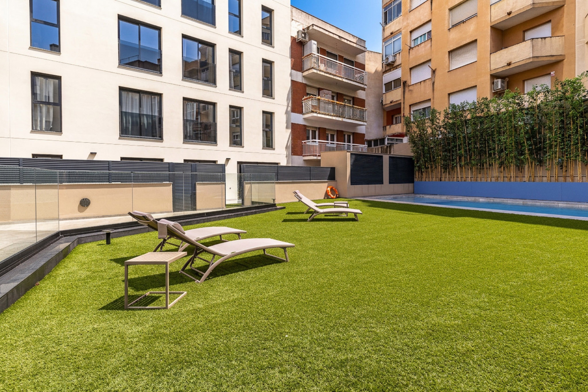 Rooftop terrace with artificial grass, lounge chairs, and a small swimming pool surrounded by urban apartment buildings. [AI-generated text]