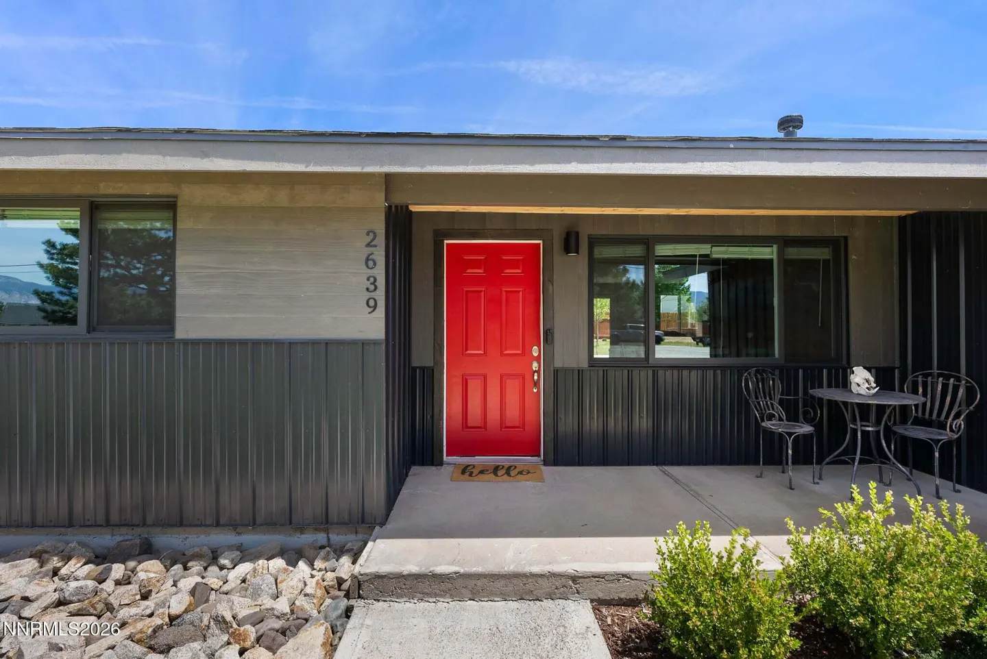 Front exterior of a house with a bright red door, address 2639, and a small patio set.