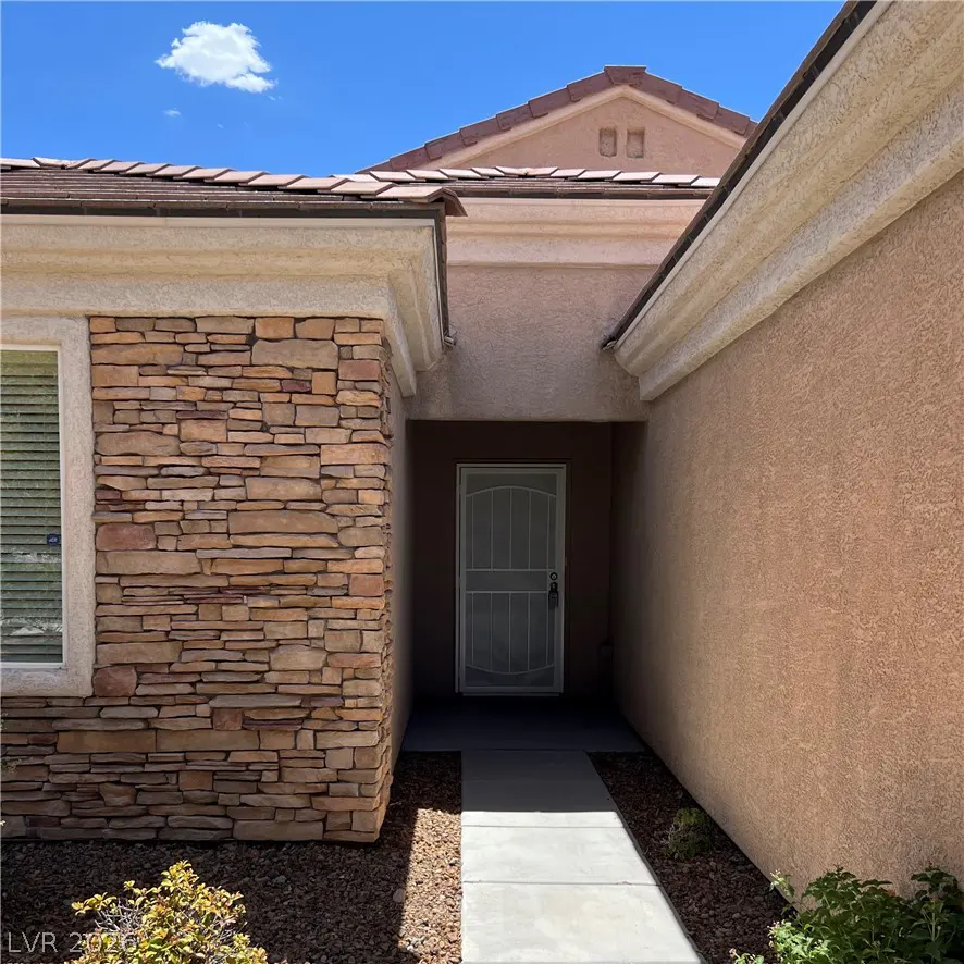 Exterior shot of a tan house with a stone facade and a white screen door under a blue sky.