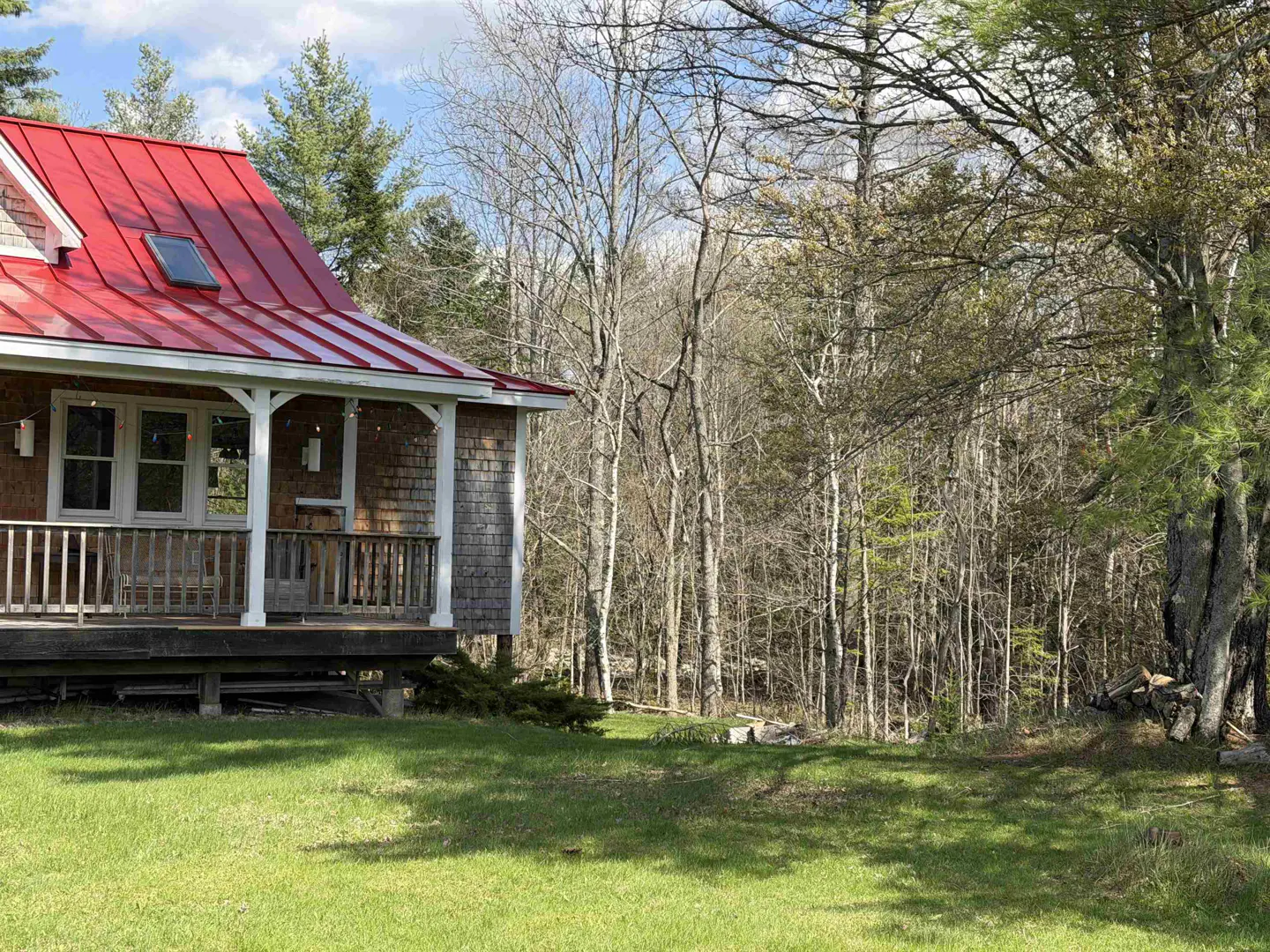 A house with a red roof and a porch, surrounded by trees and a green lawn.