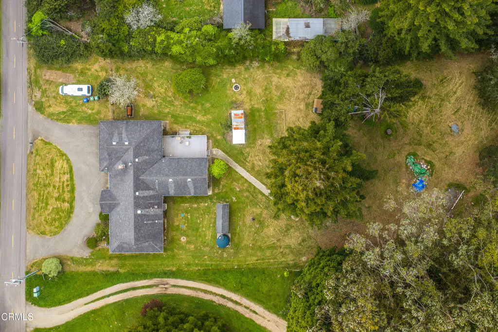 Aerial view of a gray-roofed house with a large green lawn, surrounded by trees and a road.