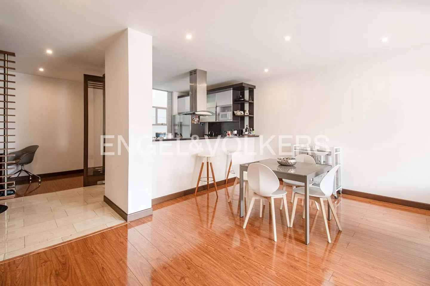 Open-concept living space with wood floors, a dining table with white chairs, and a kitchen with bar stools.