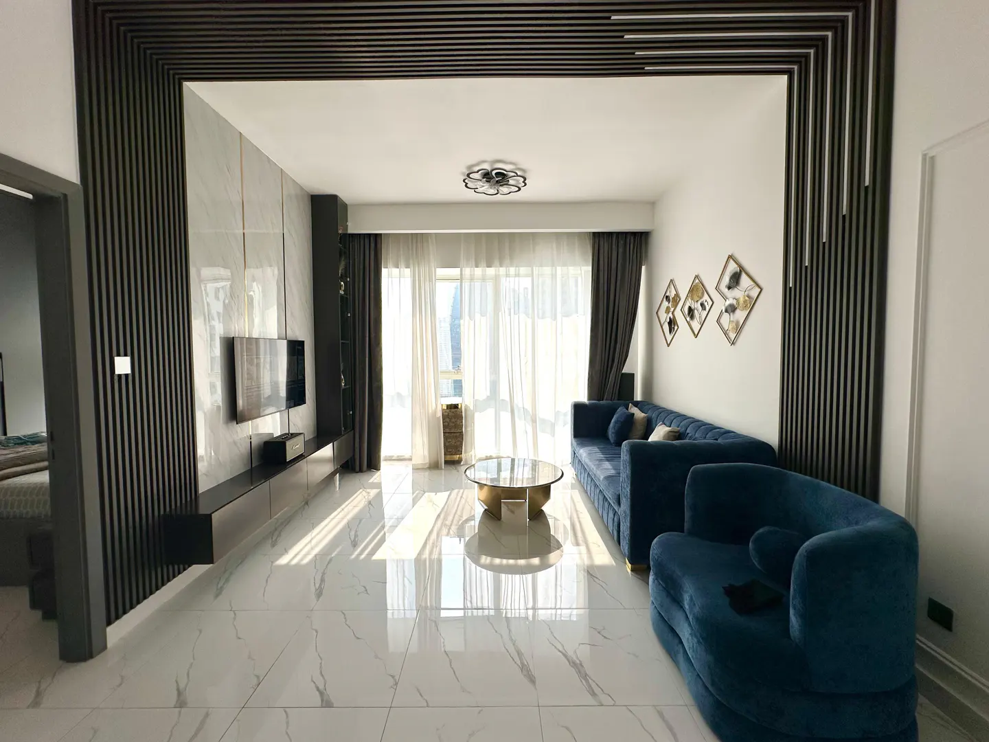 Modern living room with white marble floors, blue velvet sofa, gold coffee table, and dark wood slat wall accents.