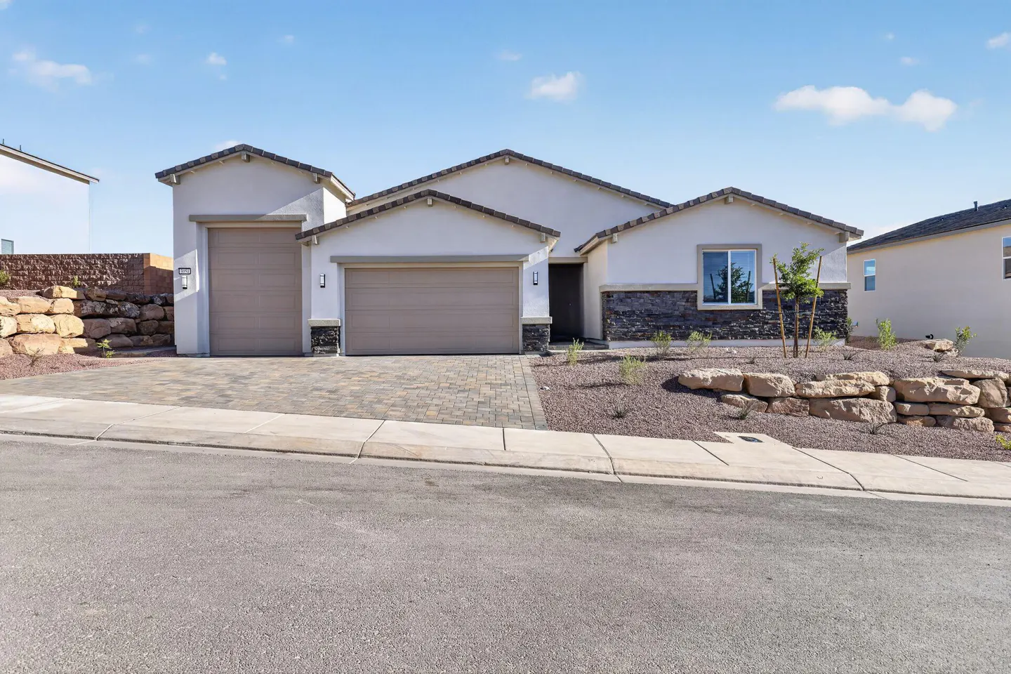 Beige stucco house with two-car garage, stone accents, and desert landscaping under a blue sky.