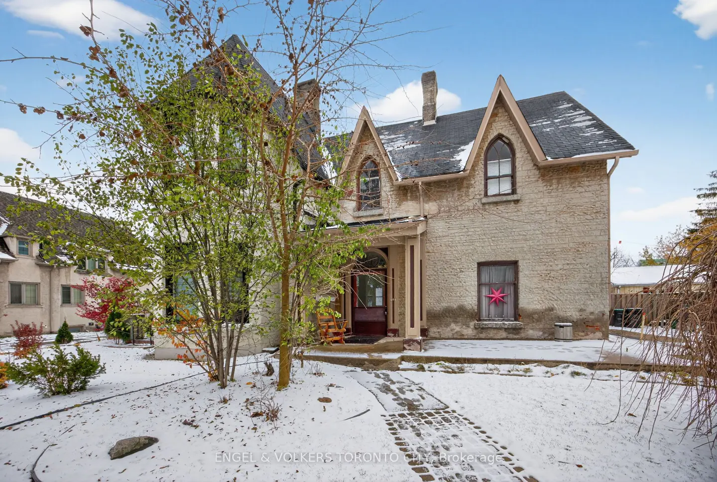 Exterior view of a two-story beige brick house with a dark roof and arched windows, surrounded by snow-covered ground and trees.