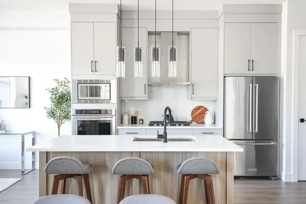 Bright kitchen with gray cabinets, stainless steel appliances, and a white countertop island with three gray stools.