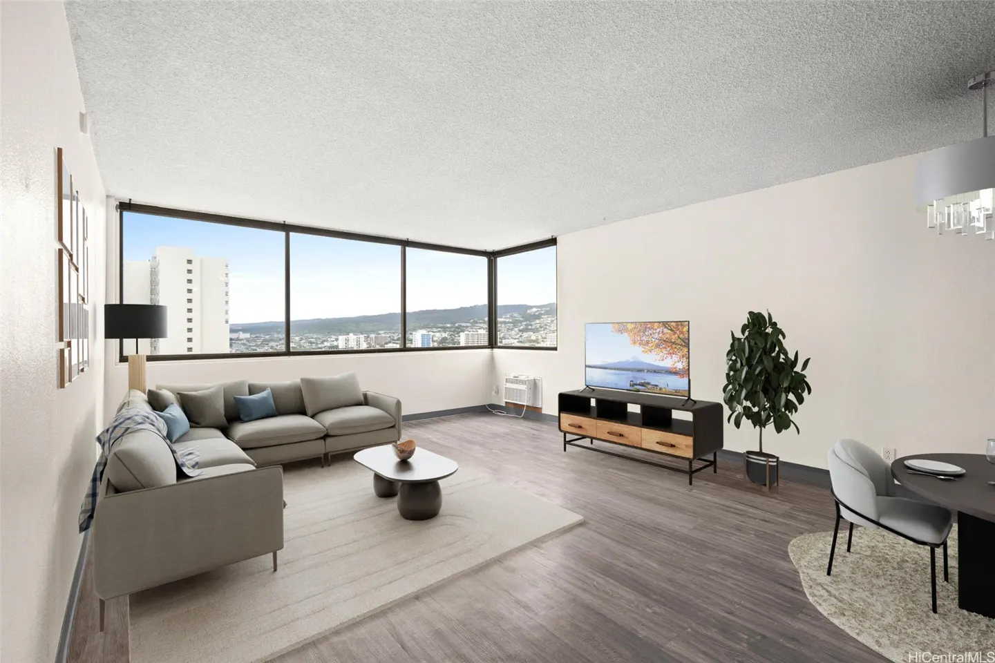 Bright living room with a gray sectional sofa, TV, and large windows with a city view.