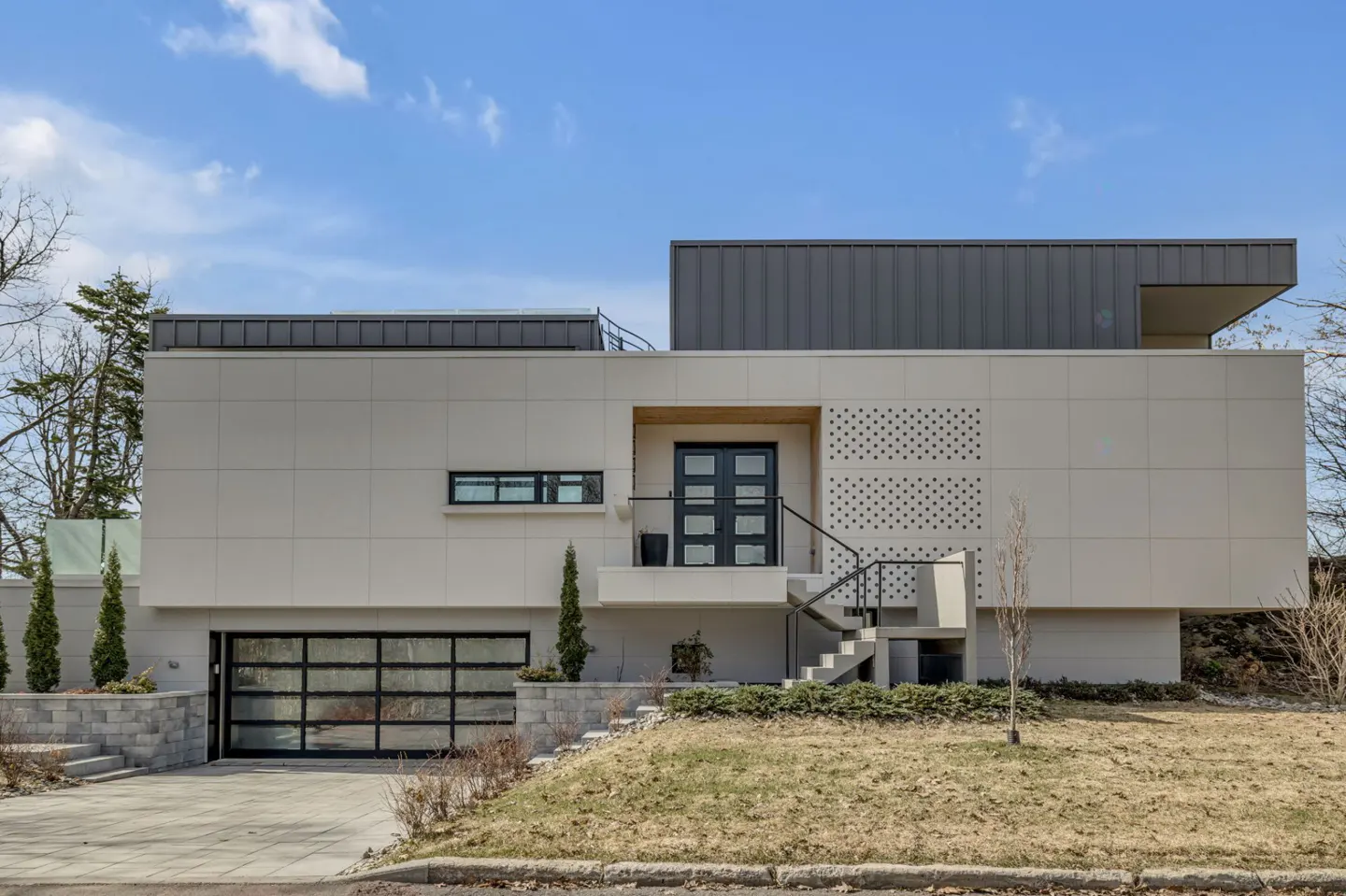 Modern beige home with a black-framed glass garage door, a black front door, and a gray metal roof against a blue sky.