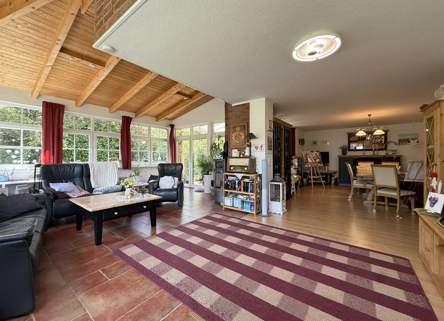 Spacious open-plan living area with a sunroom featuring a wood-beamed ceiling, tile floors, and a dining area beyond.