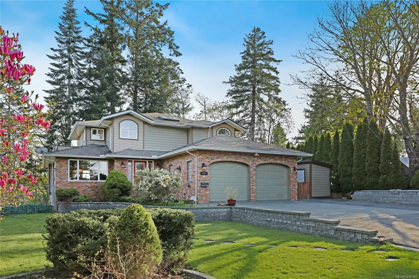Two-story house with brick and siding, two-car garage, green lawn, and trees under a blue sky.