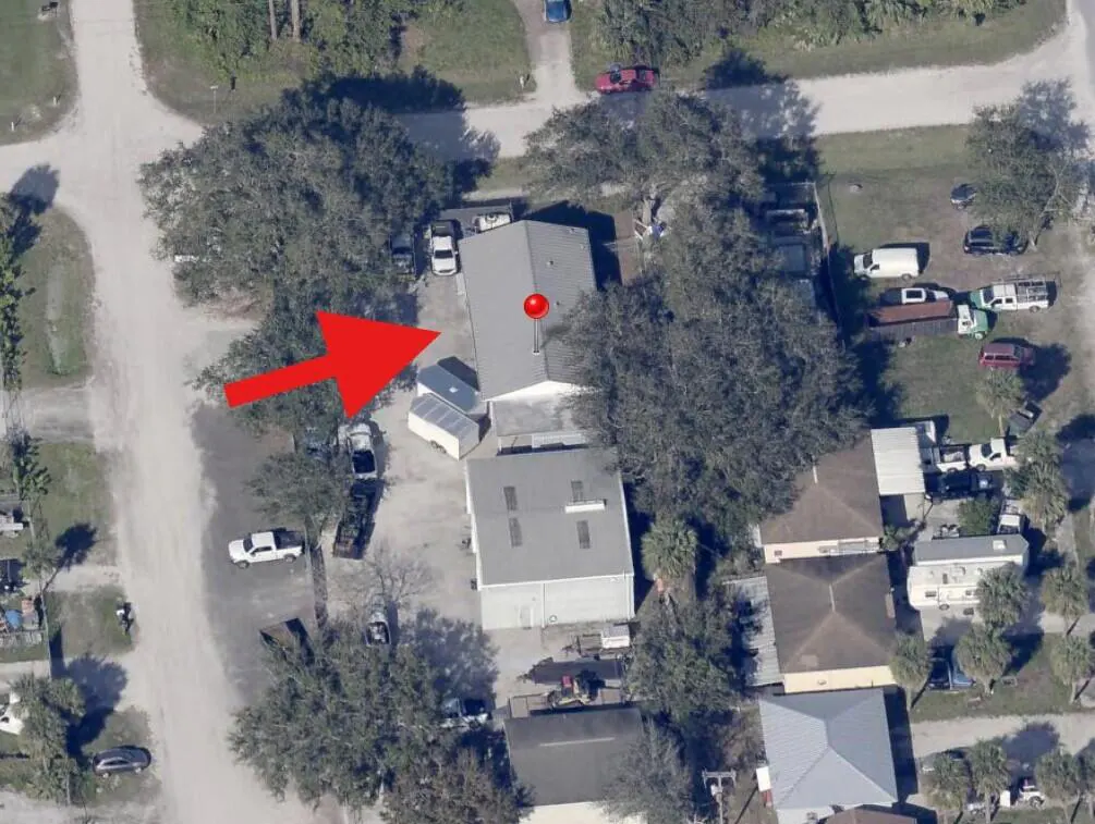 Aerial view of a property with a gray roof, indicated by a red arrow. Trees surround the building, and several cars are parked nearby.
