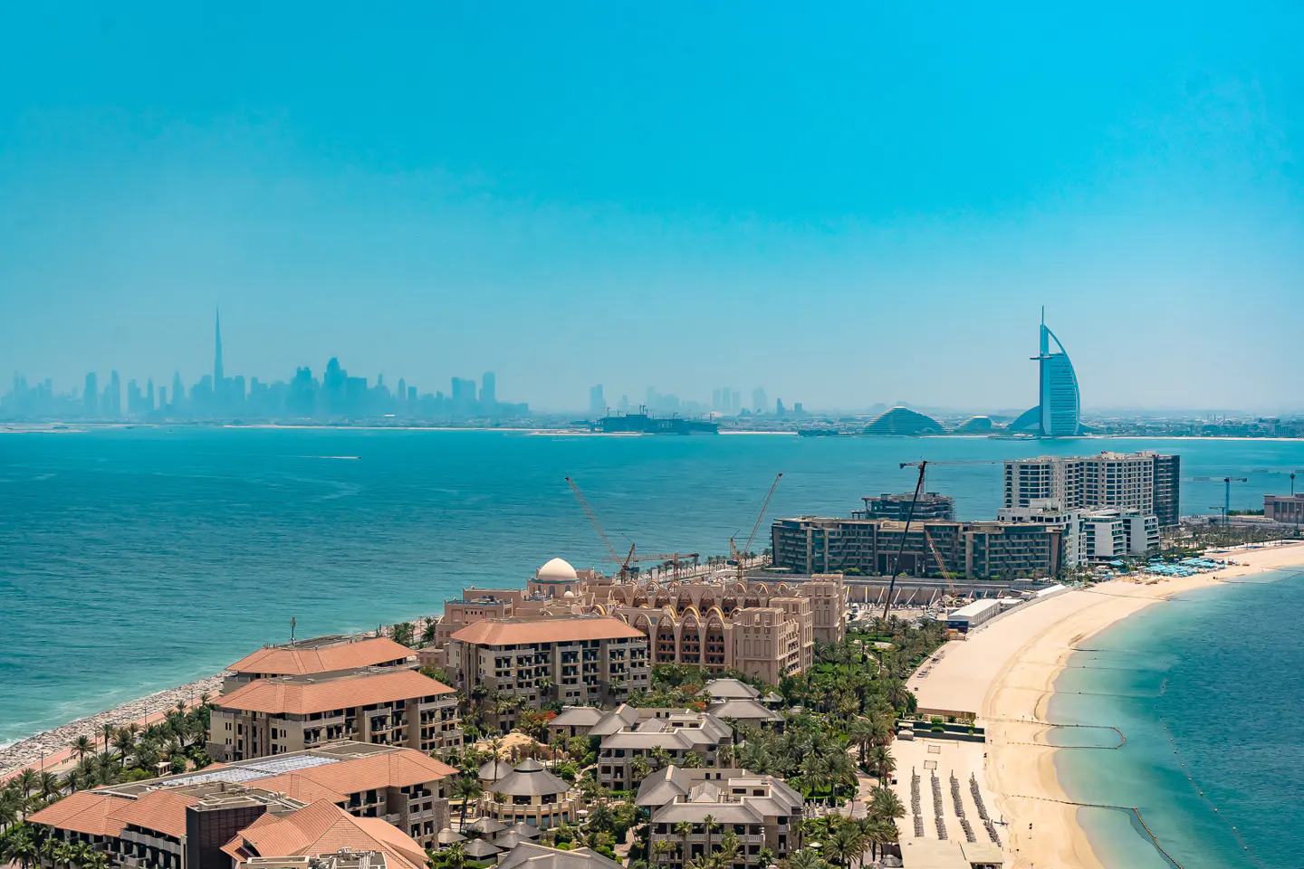 Dubai skyline view. Burj Al Arab and city buildings on the coast, with blue sea and sky.