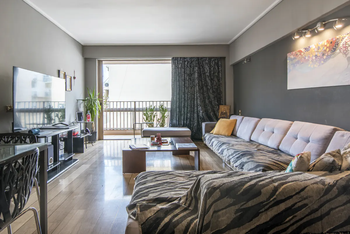 Modern living room with a large grey sectional sofa, wooden coffee table, TV, and balcony access with dark curtains.