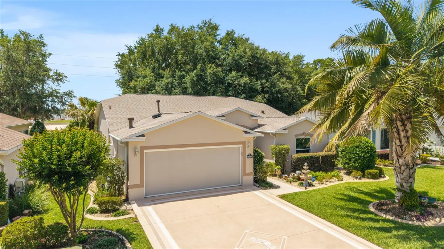Beige single-story house with a brown roof, a two-car garage, and a palm tree in the front yard.