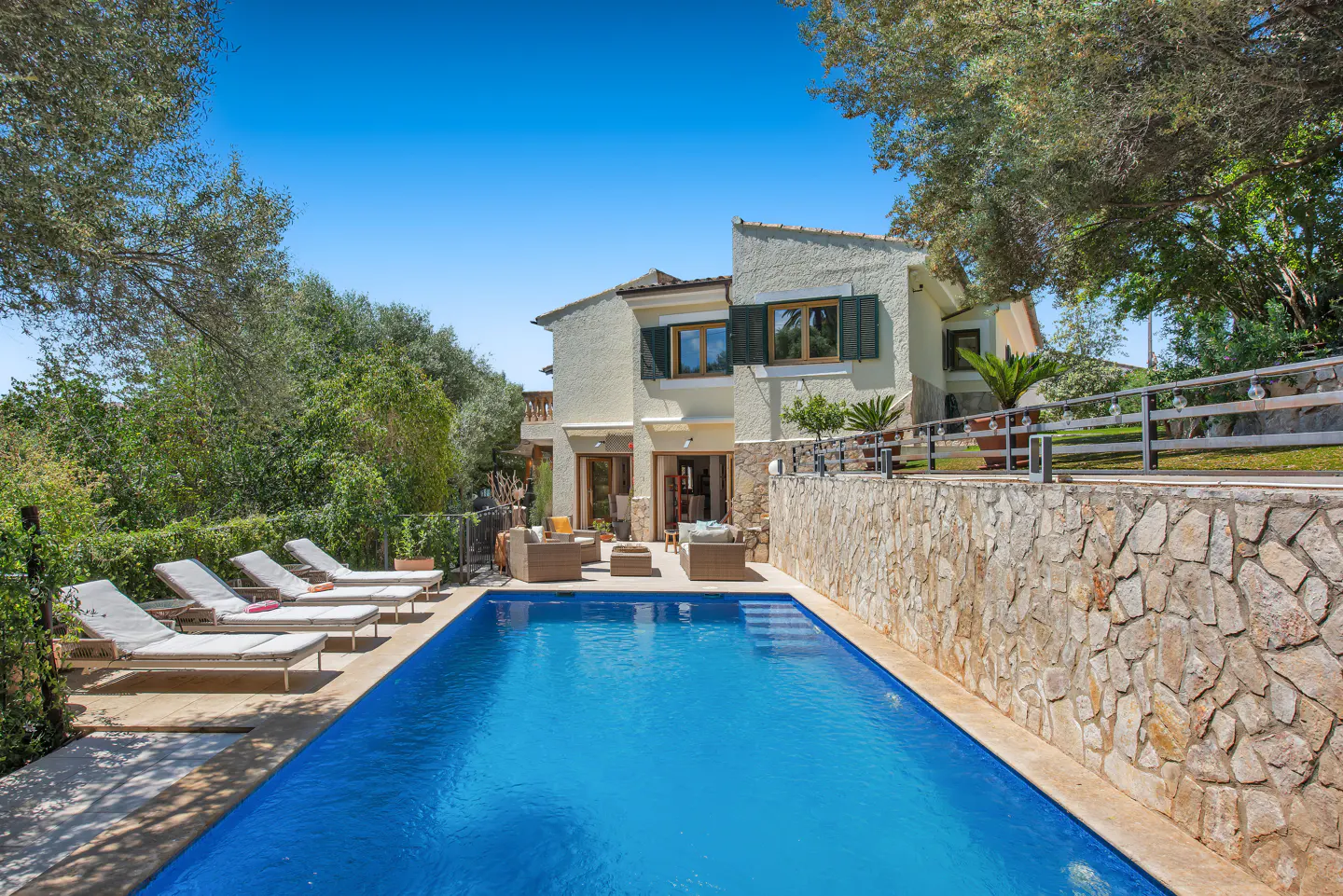 A two-story villa with a blue swimming pool, lounge chairs, and outdoor seating.