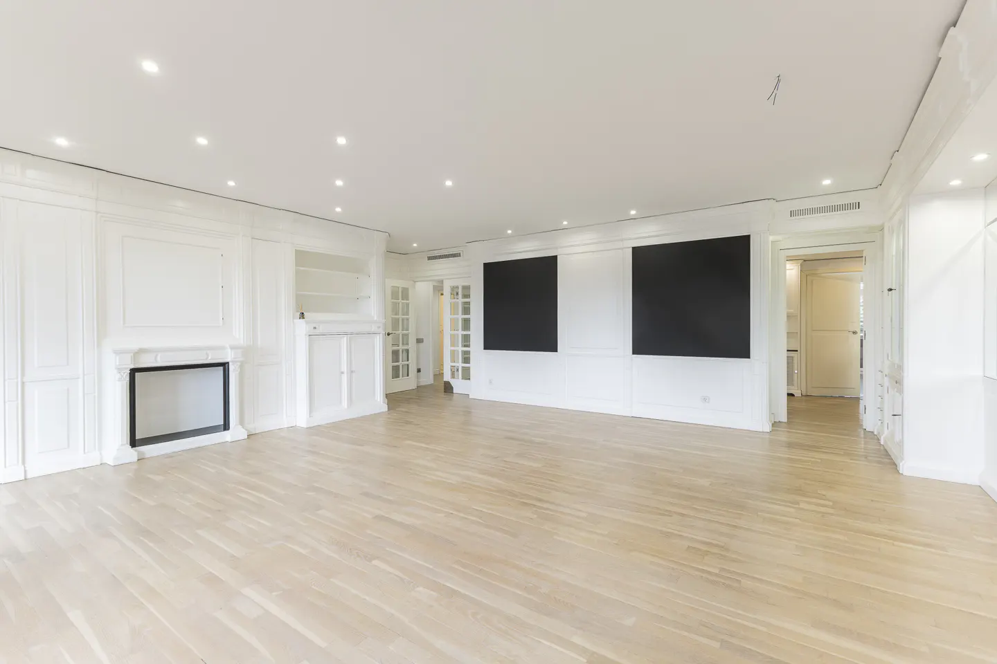 Bright, empty living room with light wood floors, white walls, fireplace, and two large black squares on the wall.