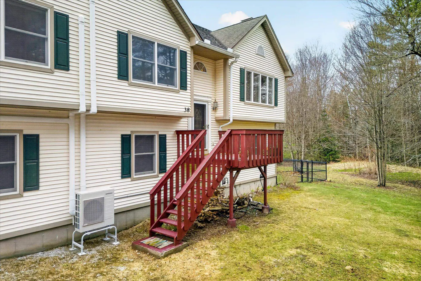 Exterior view of a two-story house with beige siding, green shutters, and a red wooden deck and stairs.