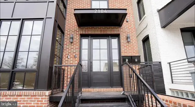 Brick townhouse with black trim, a black awning with "2104" above a black front door, and black metal stairs and railings.