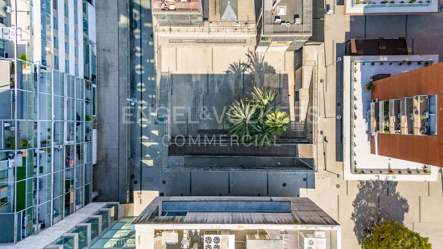 Aerial view of commercial buildings with glass facades, concrete walkways, and rooftop gardens in an urban setting.