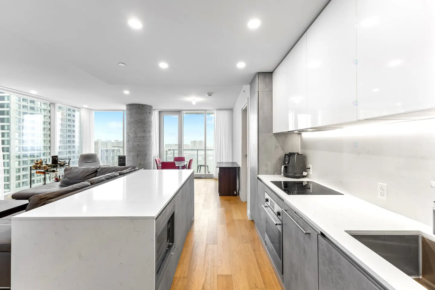 Modern kitchen with white cabinets, grey lower cupboards, white quartz island, and hardwood floors overlooking city views.