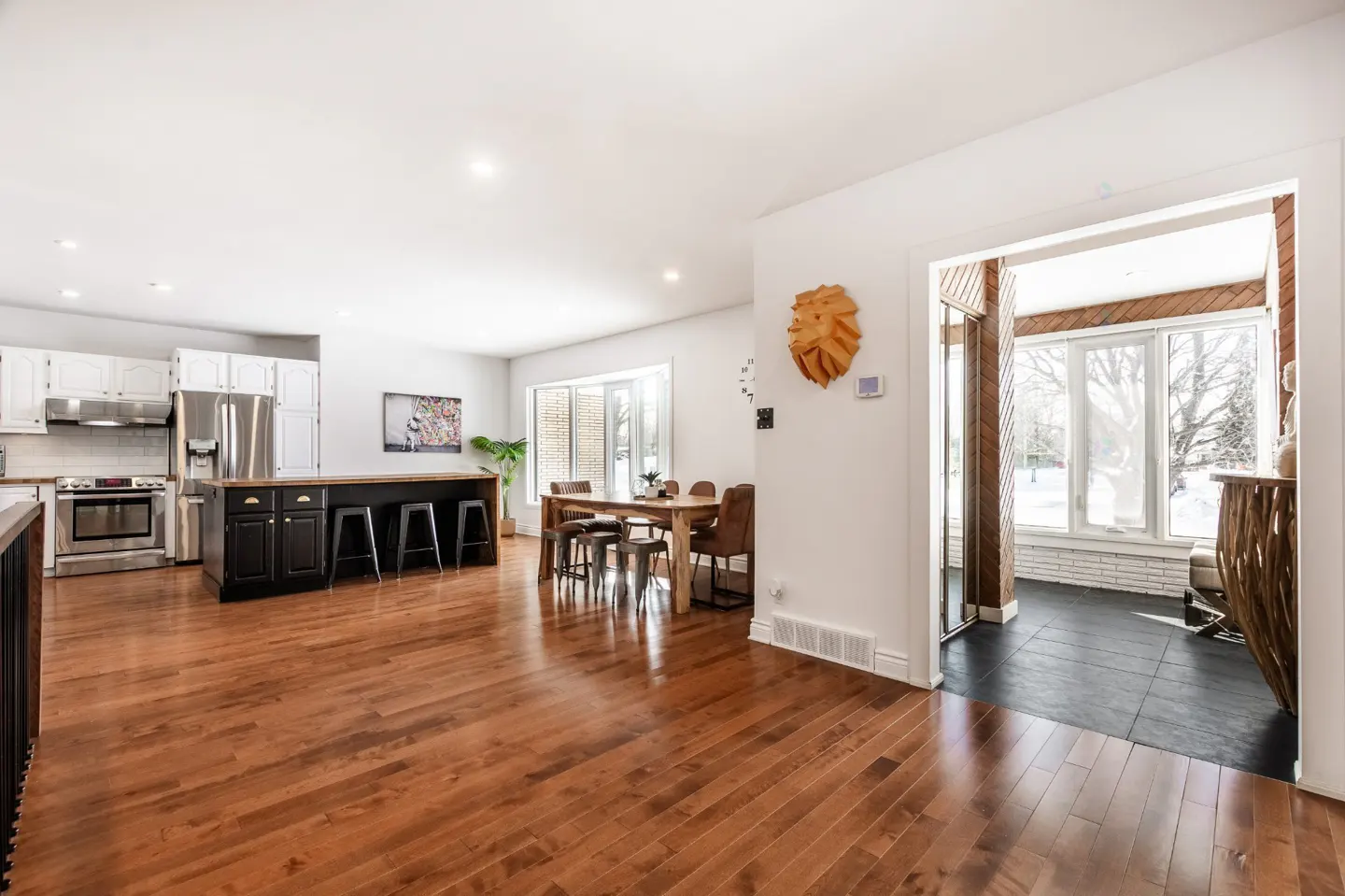 Open-concept home with hardwood floors, white walls, and a black kitchen island with bar stools. A dining table and sunroom are visible.