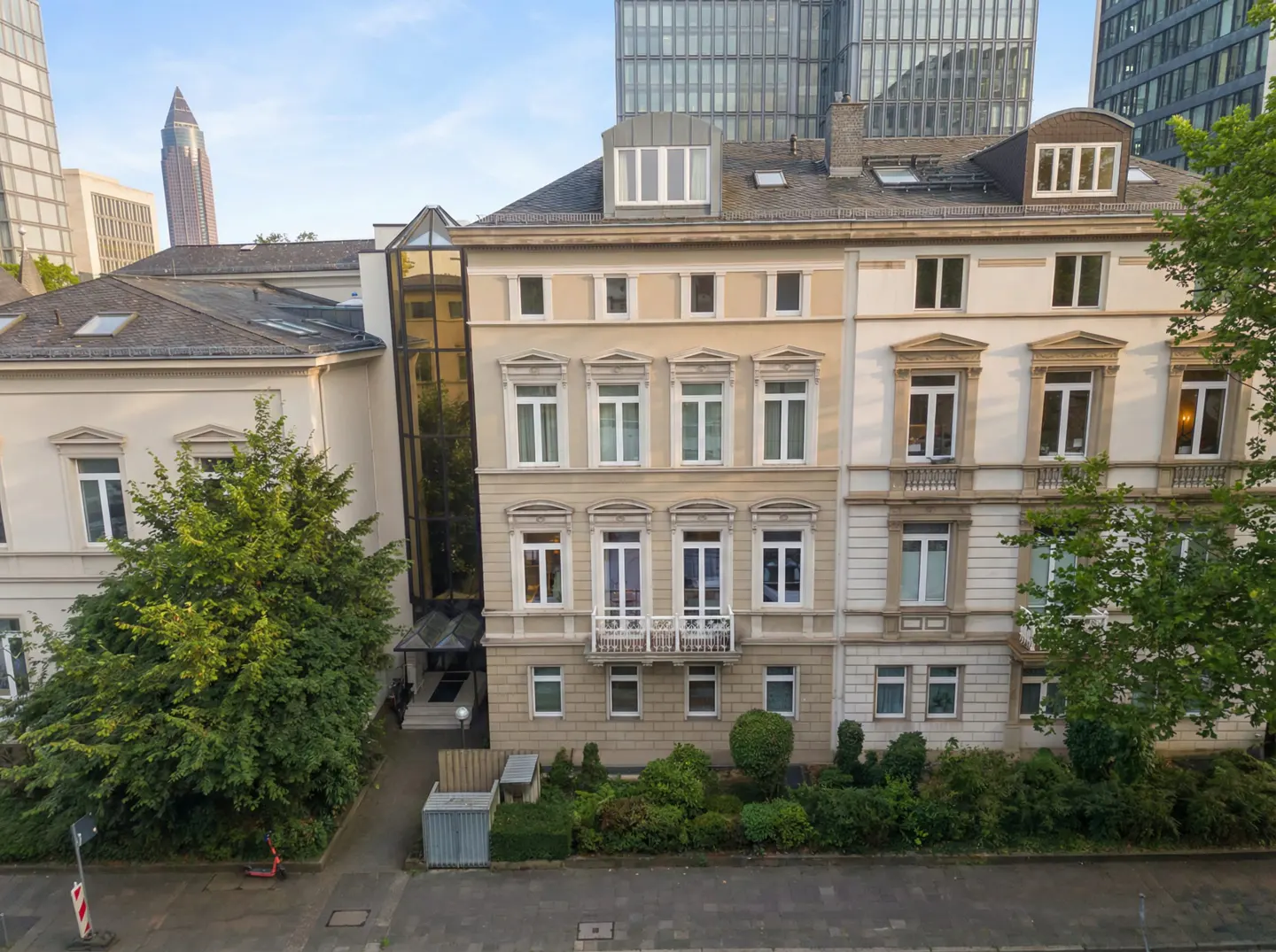 Exterior view of a beige, multi-story building with white-framed windows, set against a backdrop of modern skyscrapers.
