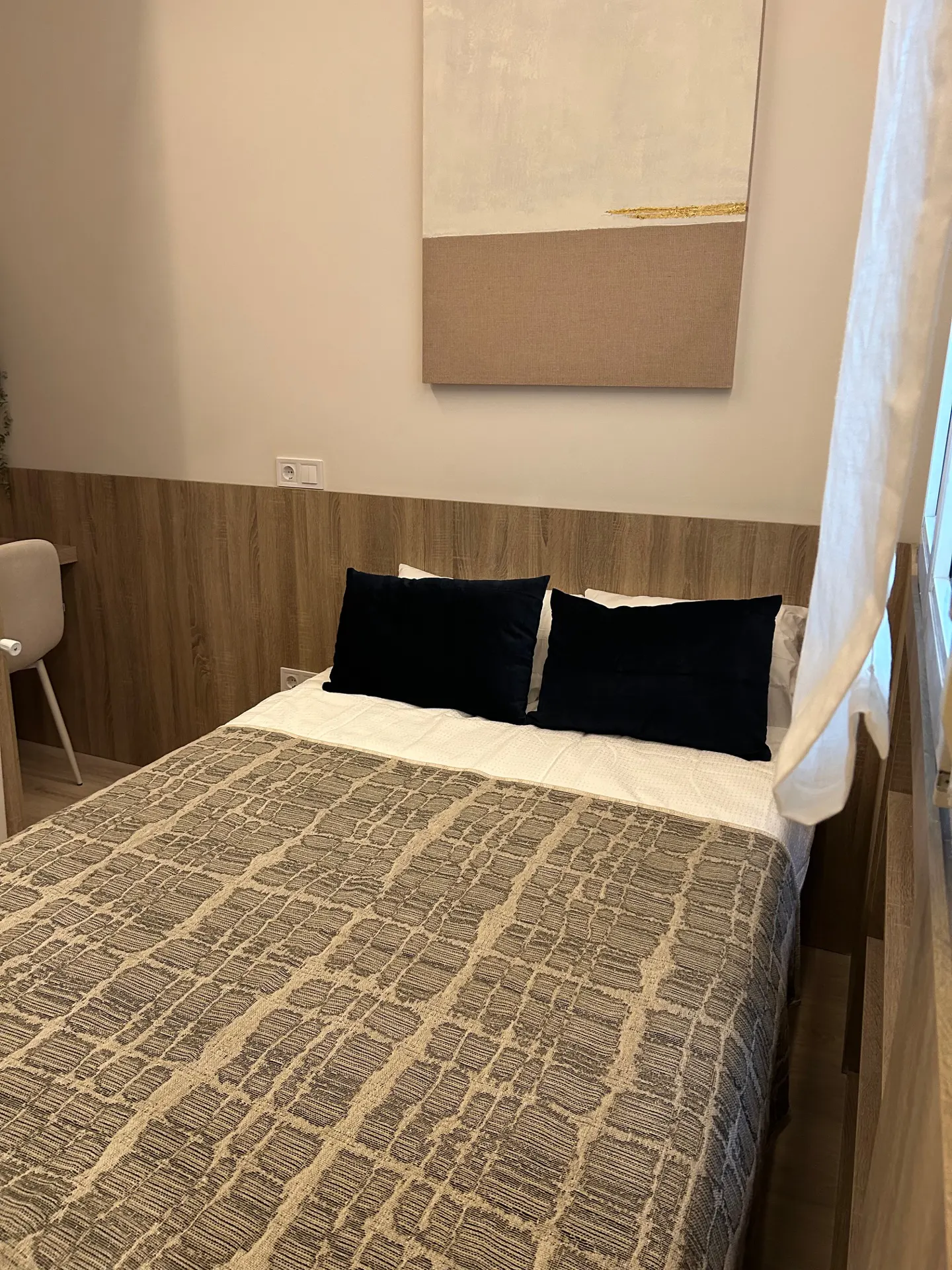 Bedroom with a queen-size bed, black pillows, and a patterned brown and beige blanket. A painting hangs above the bed.