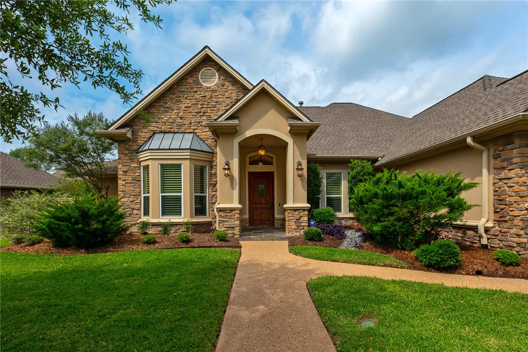 Exterior of a stone and stucco home with a brown roof, green lawn, and a winding walkway to the front door.