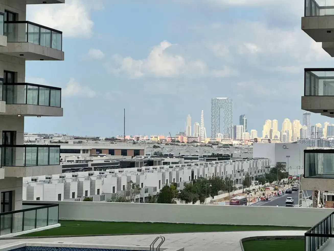 View from a balcony overlooking white townhouses and the Dubai skyline under a cloudy sky.