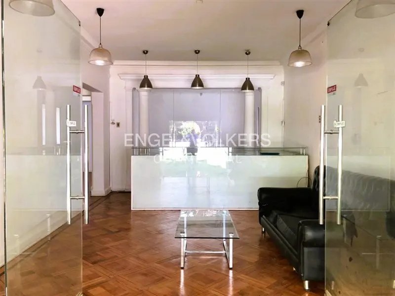 Office interior with glass doors, a white reception desk, a black leather sofa, and a glass coffee table on a parquet floor.