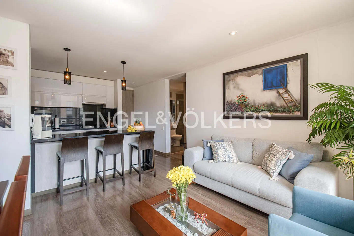 Open concept living space with kitchen island, gray sofa, blue armchair, and wood floors. A painting hangs above the sofa.