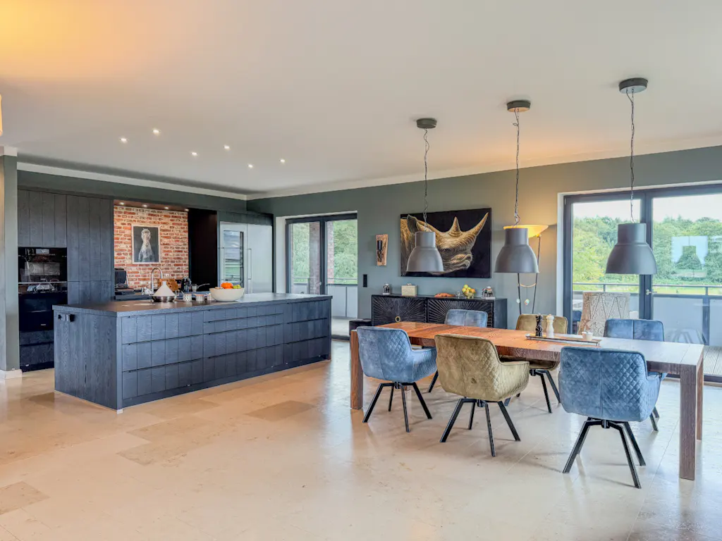 A modern kitchen and dining area with a large island, wood table, blue chairs, and pendant lights.