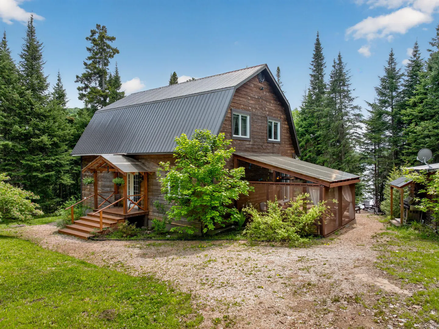 Rustic brown barn-style home with a metal roof, wooden porch, and screened-in deck, surrounded by lush pine trees.