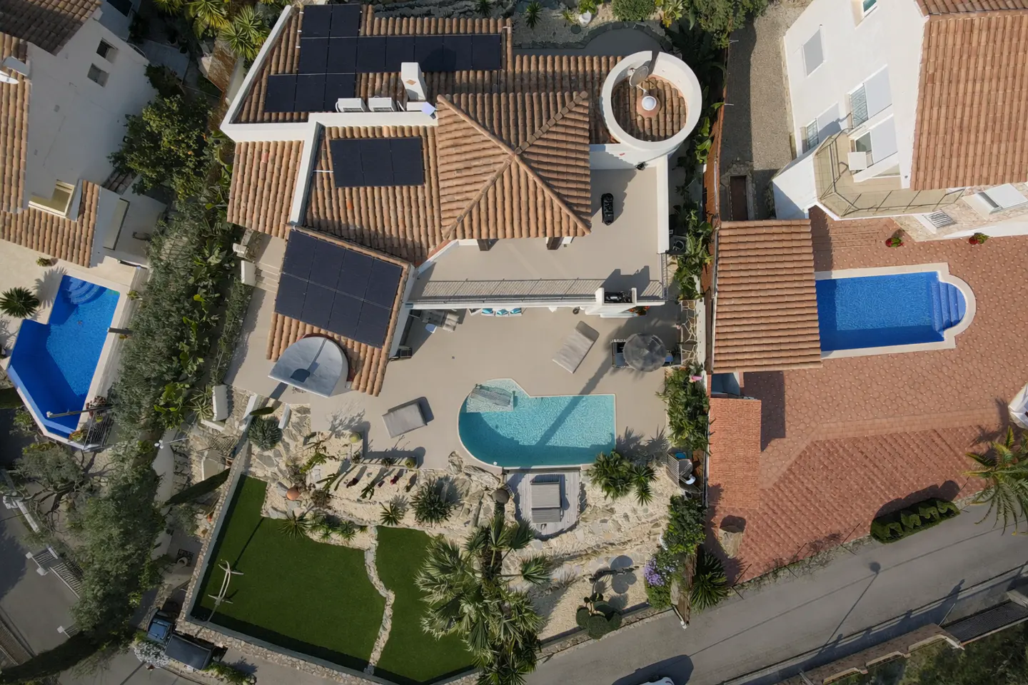 Aerial view of a villa with terracotta roof tiles, solar panels, a private swimming pool, and a landscaped garden.
