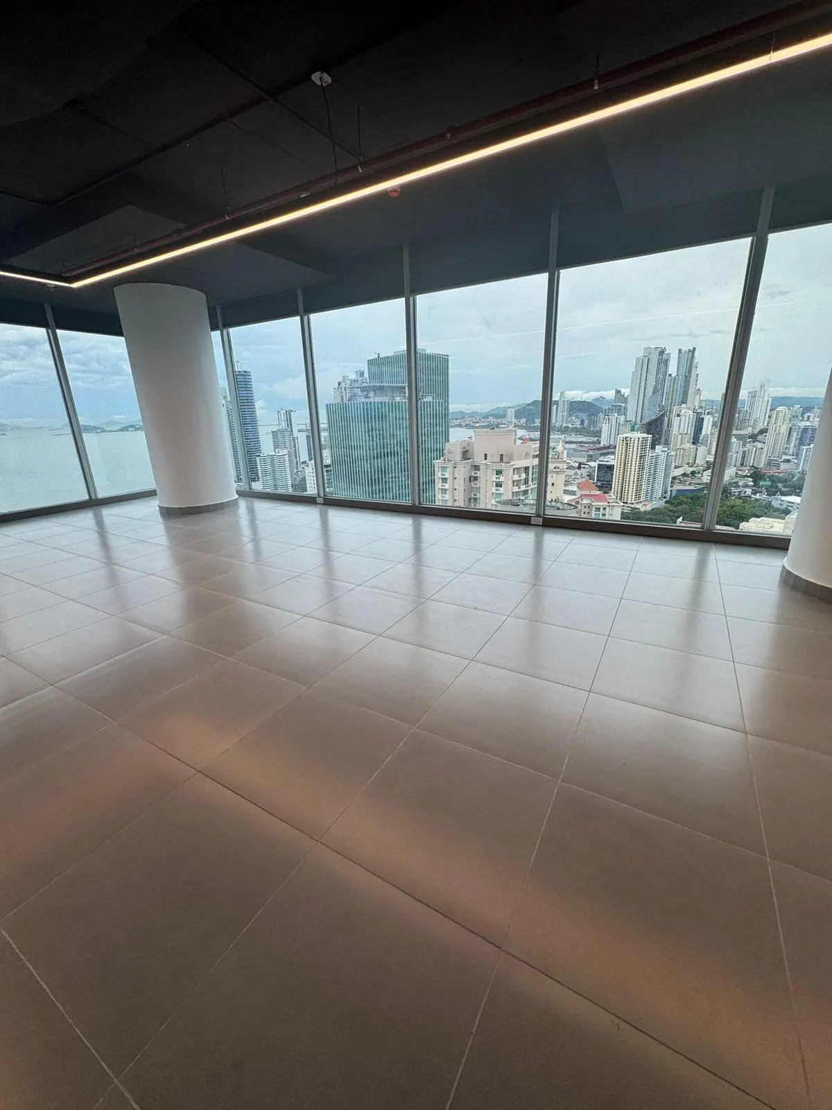 Empty office space with brown tile floor and floor-to-ceiling windows. City skyline and ocean visible through the windows.