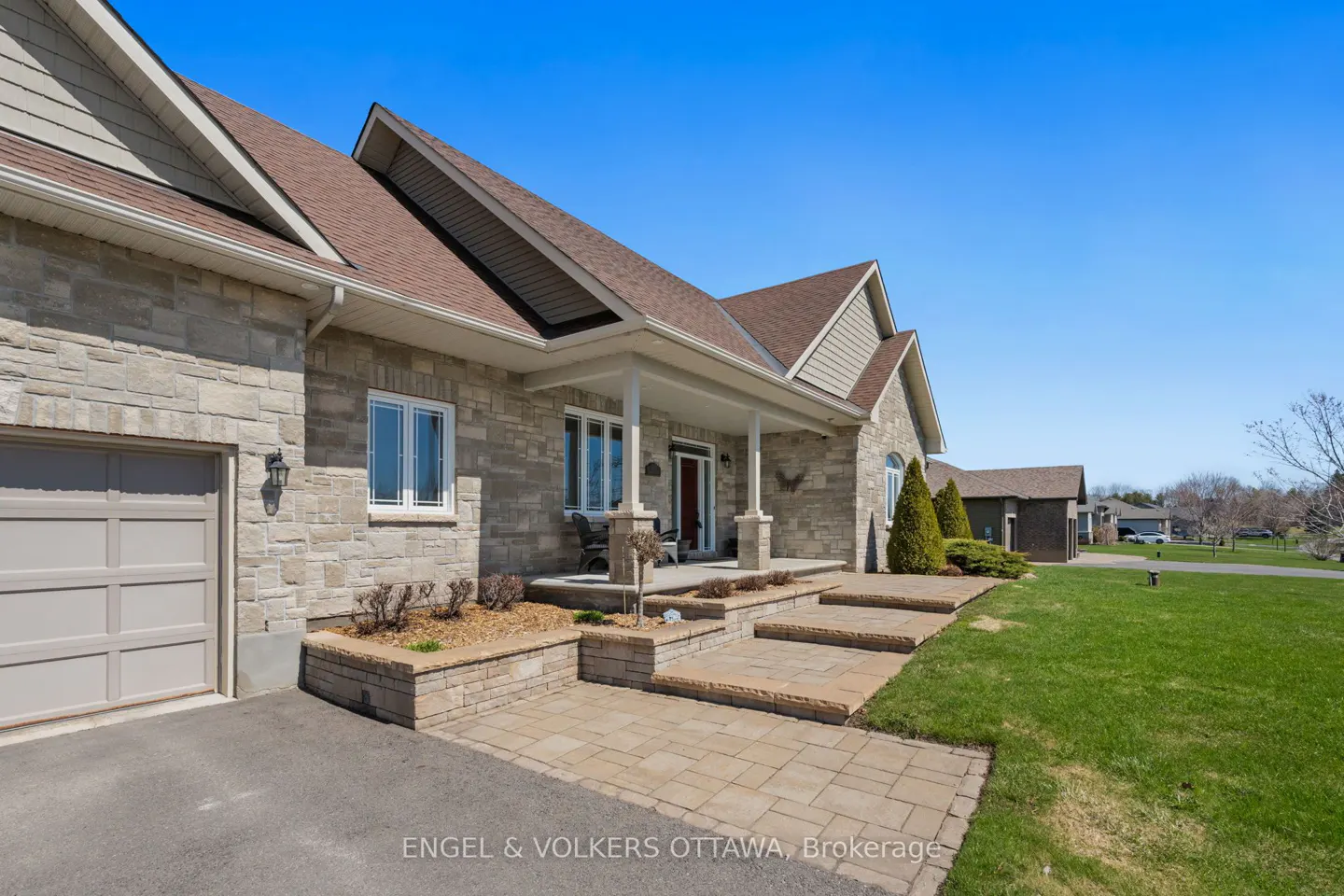 Exterior view of a stone house with a brown roof, a covered porch, and a green lawn under a clear blue sky.