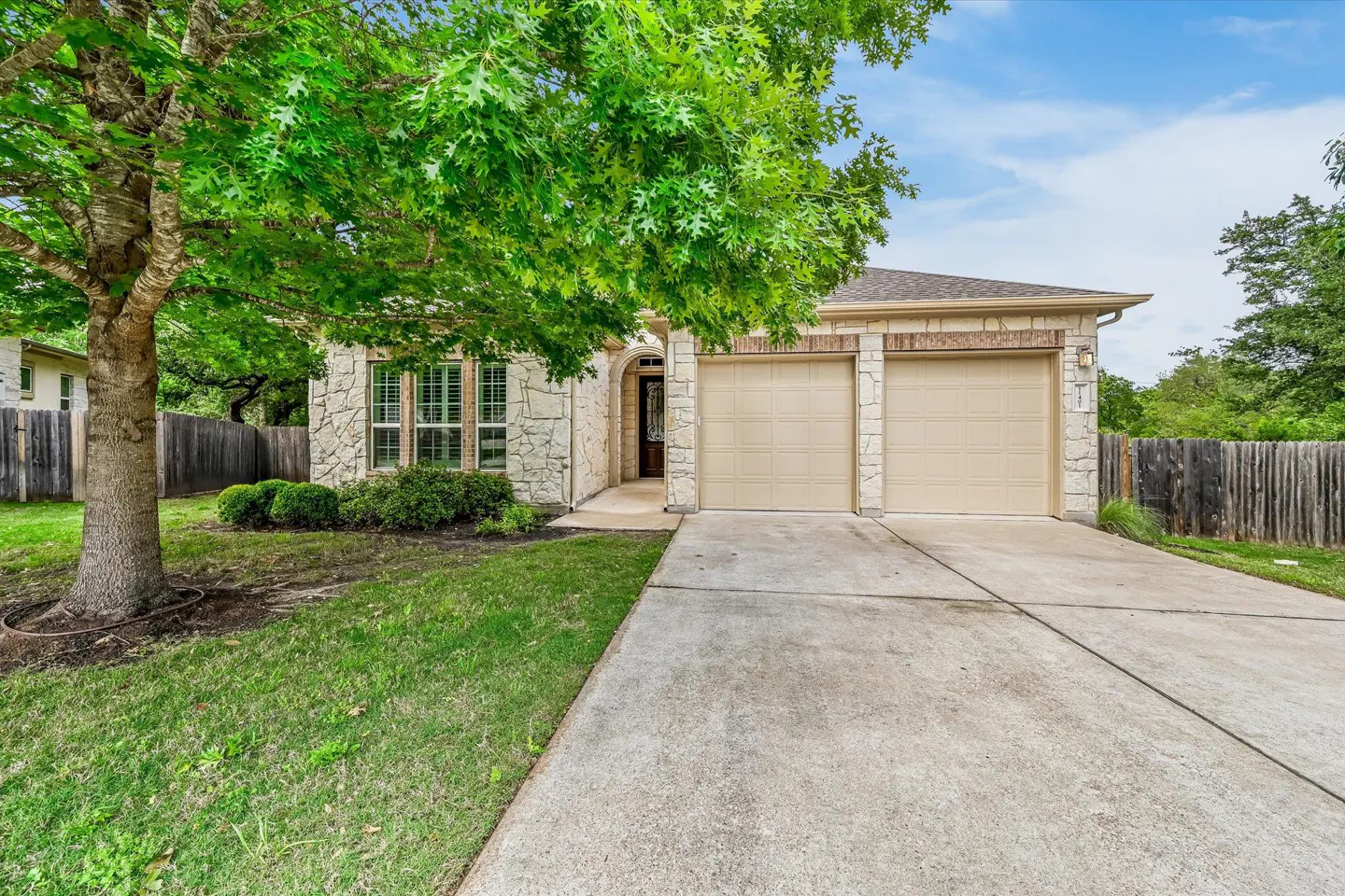 A single-story house with a stone facade, a two-car garage, and a green lawn.