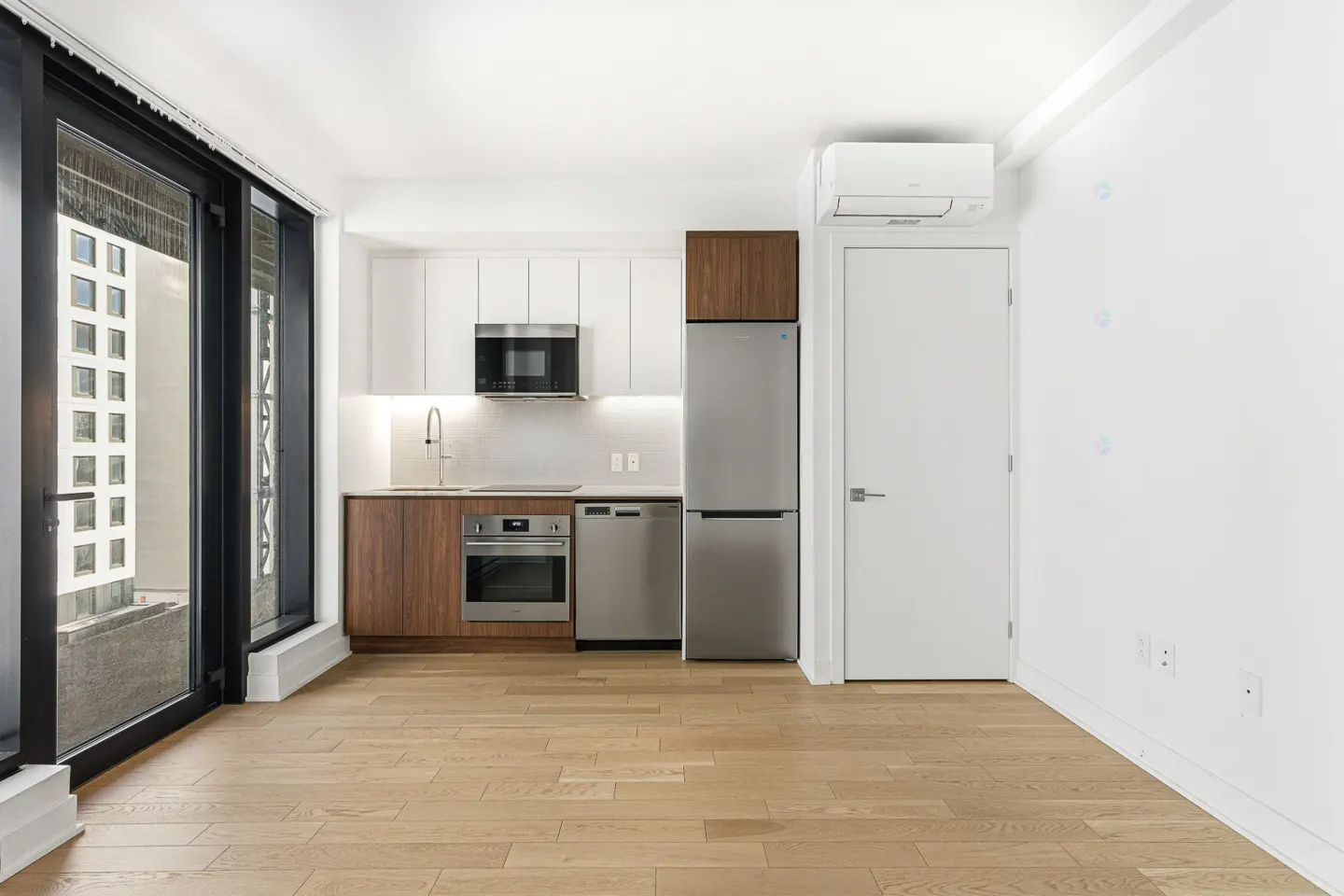 Modern kitchen with white upper cabinets, wood lower cabinets, stainless steel appliances, and light wood flooring.