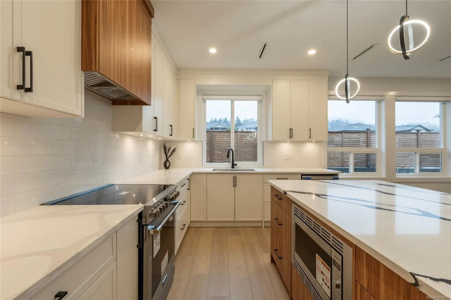Bright kitchen with white cabinets, wood accents, and stainless steel appliances. Island with marble countertop and modern pendant lights.