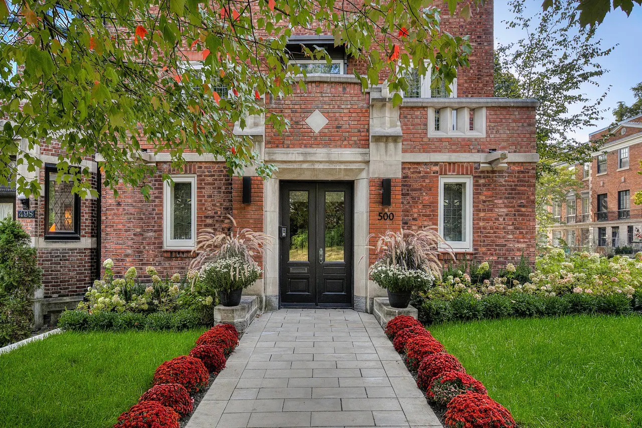 Brick house with black double doors and the number 500 above. A stone path leads to the entrance, lined with red flowers.