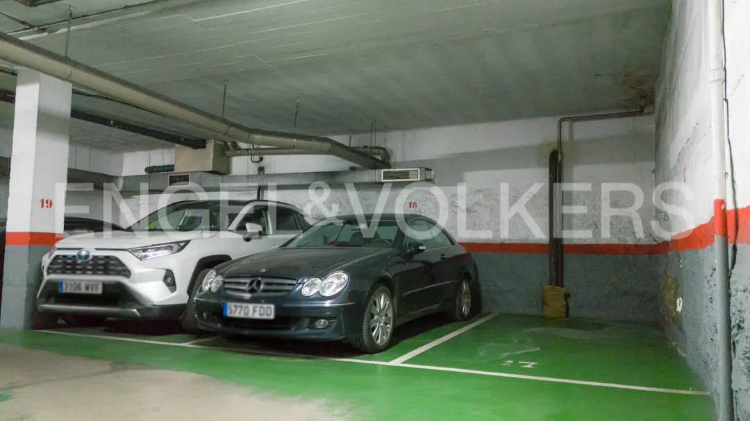 Indoor parking garage with a white Toyota SUV and a dark gray Mercedes parked in green-painted parking spaces.